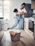 Busy mom holding baby while on phone and doing laundry.