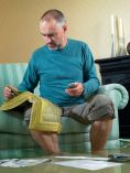 Man sitting in living room with phone book and flood water is halfway up his shin.