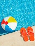 Pool with beach ball in it and flip flops next to it.