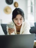 Woman holding phone and studying laptop.