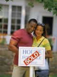 Couple holding SOLD sign in front of house.