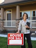 Realtor next to For Sale sign in front of house.