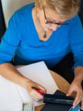 Woman writing things down. Calculator in one hand.