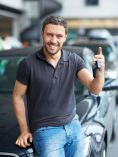 Man sitting on a car holding up car keys.