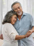 Older Asian couple slow dancing in living room.