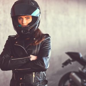 Woman in motorcycle gear in front of motorcycle.