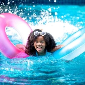 Little girl swimming in a pool with two float toys.