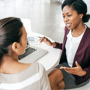 Two women sitting in front of laptop talking.