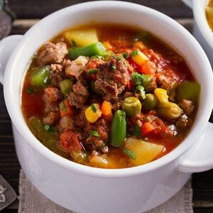 Photo of a bowl of hamburger soup with tomatoes, potatoes, corn, peas, etc.