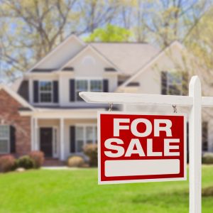 Photo of a for sale sign in the front yard of a house.