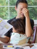 Stressed mom paying bills with toddler on lap.