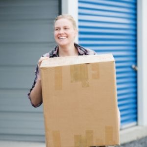 Woman carrying box in front of storage facility that has blue doors.